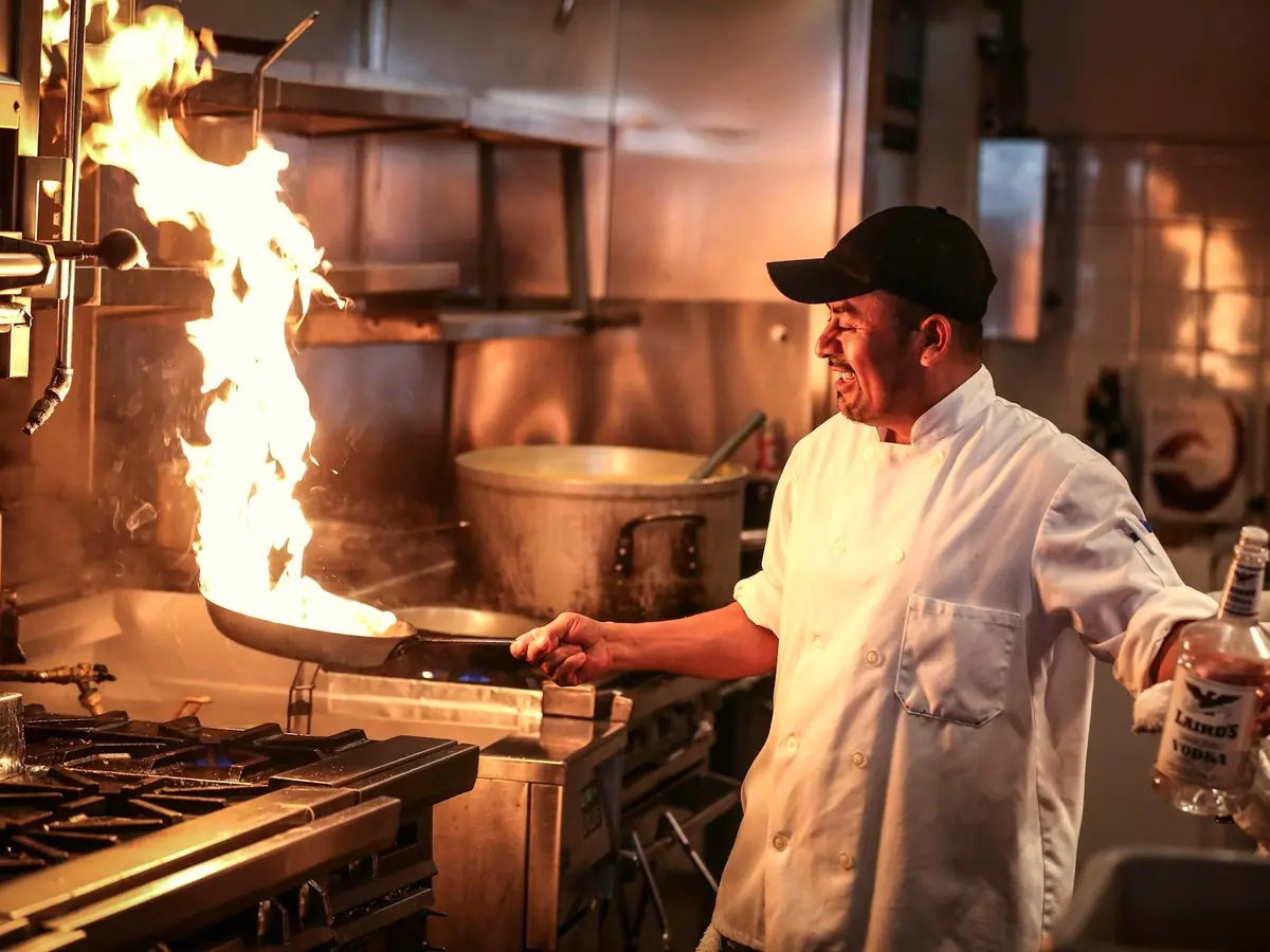 Chef laughing at the stove as a pan flames up